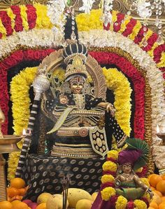 an idol sitting on top of a table surrounded by fruit and flowers in front of it