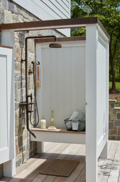 an outdoor shower on a wooden deck next to a brick wall and tree in the background