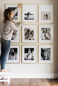 a woman is standing on a stool in front of a wall with many pictures hanging on it