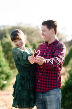 a man and woman standing next to each other in front of christmas trees holding scissors