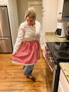 a woman in a red and white checkered apron is looking down at the floor