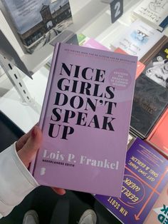 a person holding up a purple book in front of bookshelves with the words nice girls don't speak up