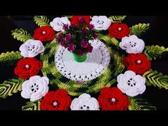 a crocheted doily with red and white flowers in the center, surrounded by green leaves