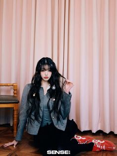 a woman sitting on the floor in front of a chair with long black hair and bangs