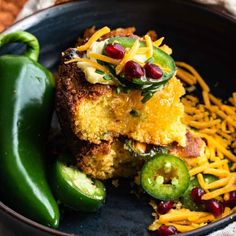 a black plate topped with cornbreads and green peppers next to cheese covered chilies