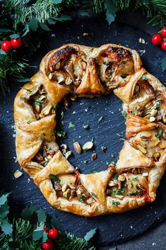 a pastry with nuts and other toppings on a black surface surrounded by holly leaves