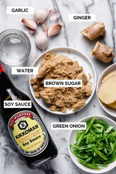 ingredients to make an apple cider recipe laid out on a marble counter top, including apples, ginger, water, brown sugar, soy sauce and green onion