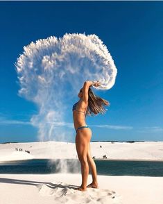 a woman standing on top of a sandy beach next to a body of water holding a white object in her hand