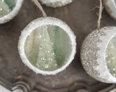 three ornaments are hanging from twine on a silver tray with white and green decorations