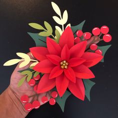 a paper poinsettia being held by someone's hand with red berries on it