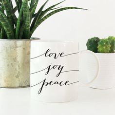 two mugs with plants in them sitting next to each other on a white table