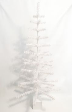 a small white christmas tree on a stand in front of a white wall with the shadow of it's branches