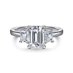 an emerald cut diamond ring with three side stones on the band and two claw prongs