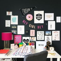 a white desk topped with lots of assorted items and posters on the black wall