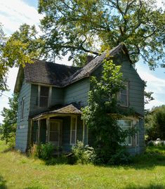 an old run down house sitting in the middle of a field with trees and grass