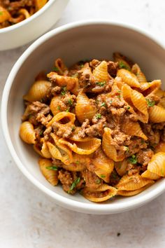 two bowls filled with pasta and meat on top of a white countertop next to each other