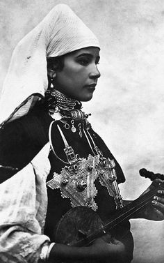 an old black and white photo of a woman with a guitar in her hands, wearing a turban