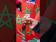 a person holding up a glass of beer in front of red and green flags with stars on them