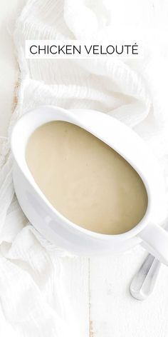 chicken veloute soup in a white bowl on a white tablecloth with spoons