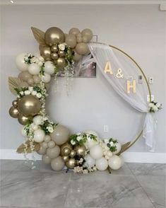 a white and gold balloon arch decorated with flowers, greenery and balloons in the shape of a circle