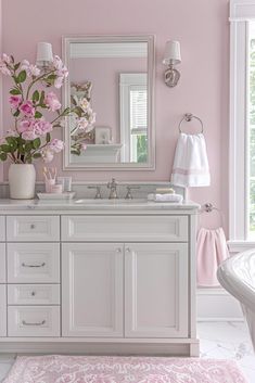 a bathroom with pink walls, white cabinets and flowers in vases on the sink