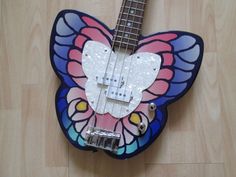 a colorful butterfly shaped guitar sitting on top of a wooden floor