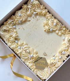 a birthday cake with white frosting and gold decorations in a box on a table