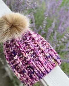 a knitted hat with a pom - pom sits on a wooden rail