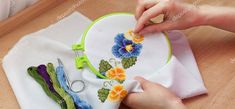 someone is using scissors to stitch flowers on a piece of white fabric with green and yellow trim