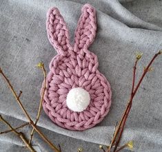 a pink crocheted bunny hat sitting on top of a gray blanket next to branches