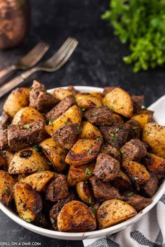 a white bowl filled with cooked potatoes on top of a table next to a fork and knife