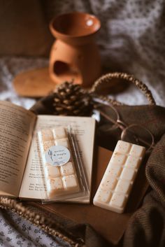 an open book sitting on top of a bed next to two pieces of wax paper