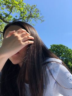 a woman holding her hand up to her head in front of a tree and blue sky