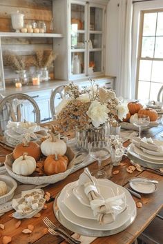 the table is set with white dishes and pumpkins