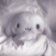 a white stuffed animal laying on top of a bed covered in blankets and sheets with eyes drawn