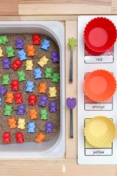 a tray filled with different colored bears next to cupcake molds