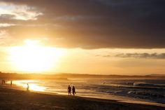 some people are walking on the beach at sunset