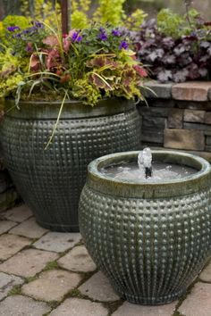 two large planters sitting next to each other on a brick patio with flowers in the background