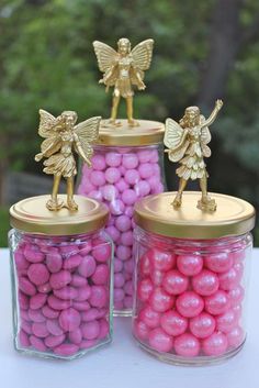 three jars filled with pink and yellow candies next to gold fairy figurines