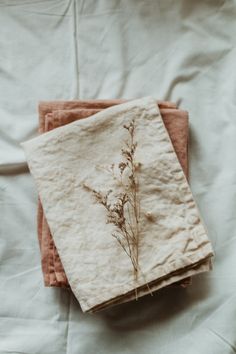 two napkins with dried flowers on them sitting on a white bed linen covered sheet