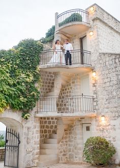 a bride and groom standing on the balcony of a stone building