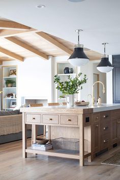 a kitchen island in the middle of a living room with two lamps hanging above it