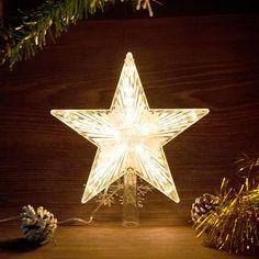 a lighted christmas star sitting on top of a wooden table next to pineconis