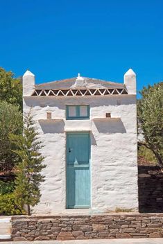 a white building with a blue door and window on the side of it, surrounded by trees