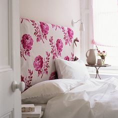 a bed with white sheets and pink flowers on the headboard is in front of a window