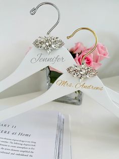 a white hanger with two pairs of earrings on it and a pink rose in the background