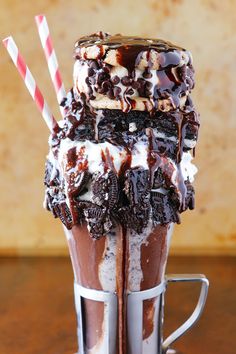 a chocolate milkshake with ice cream and oreo cookies on top, sitting in a coffee cup