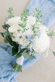 a bouquet of white flowers and greenery on a blue cloth draped over the ground