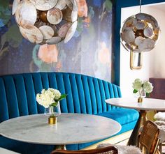 a restaurant with blue velvet booths and gold accents, white flowers in vases on the table