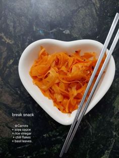 two chopsticks in a heart shaped bowl with shredded carrots on the side